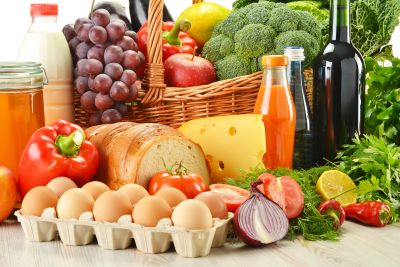 Groceries in wicker basket including vegetables fruits bakery and dairy products and wine isolated on white